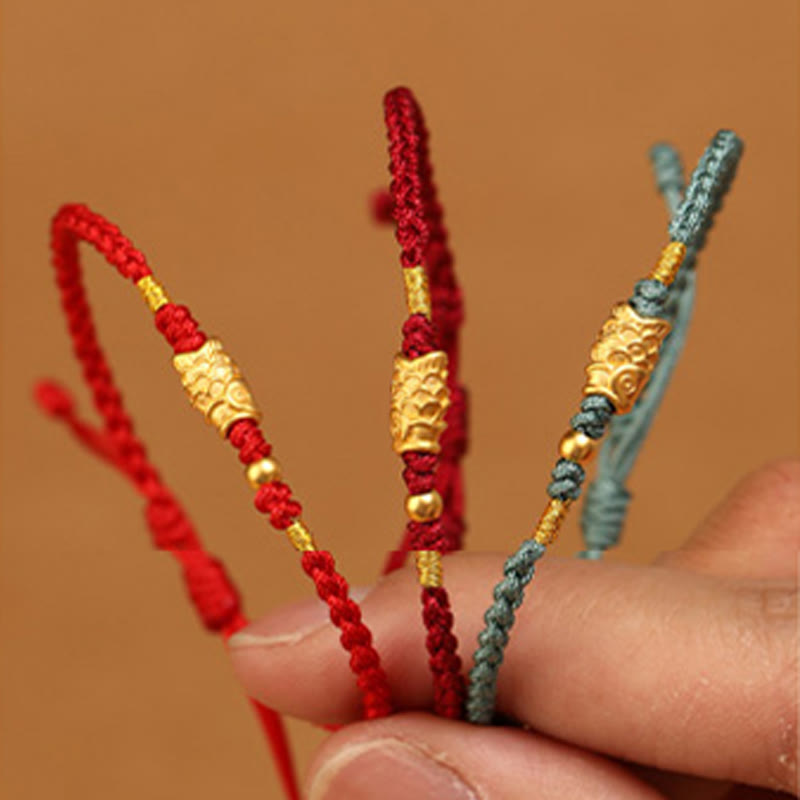 999 Gold Koi Fish Red String Bracelet – macro close-up, three bracelets with gold koi in fingers, wealth