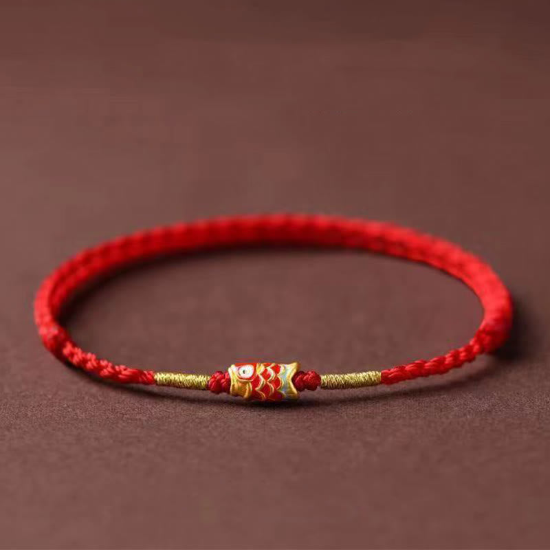 Koi Fish Braided Red String Bracelet – red cord with gold koi charm and beads, side view on brown, luck jewelry