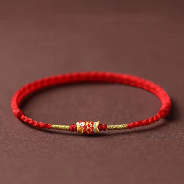 Koi Fish Braided Red String Bracelet – red cord with gold koi charm and beads, side view on brown, luck jewelry