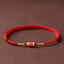 Koi Fish Braided Red String Bracelet – red cord with gold koi charm and beads, side view on brown, luck jewelry