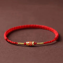Koi Fish Braided Red String Bracelet – red cord with gold koi charm and beads, side view on brown, luck jewelry