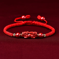 Handcrafted Cinnabar PiXiu bracelet – red braided cord with cinnabar PiXiu on dark fabric, feng shui