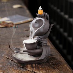 Buddha Hand Teapot Incense Burner – Stylized hands cradle cup, smoke cascading like waterfall, dark ceramic on wood