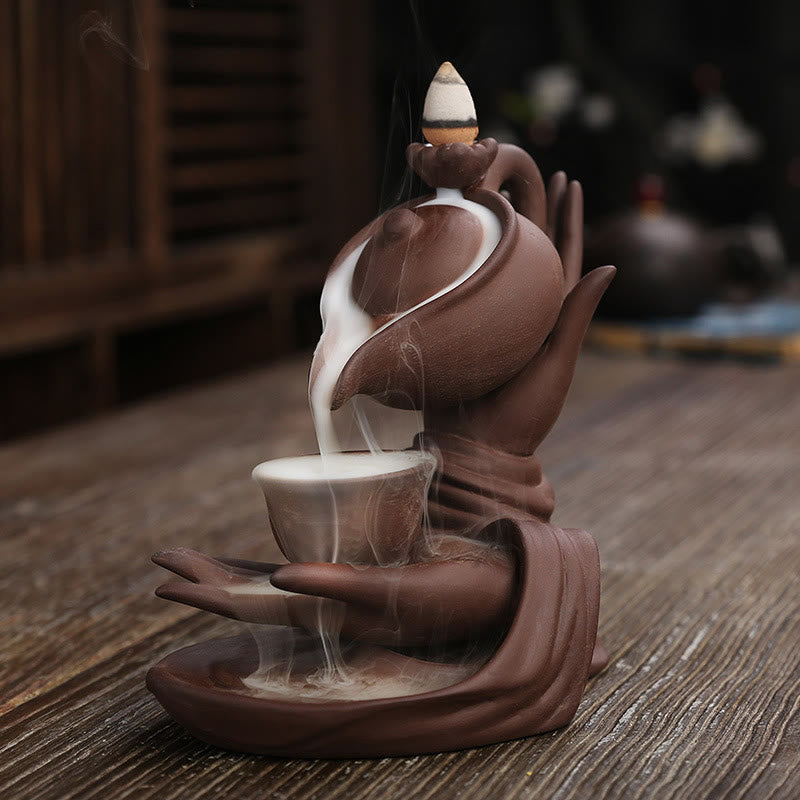 Buddha Hand Teapot Incense Burner – Terracotta teapot pours smoke into cup, hands support, backflow