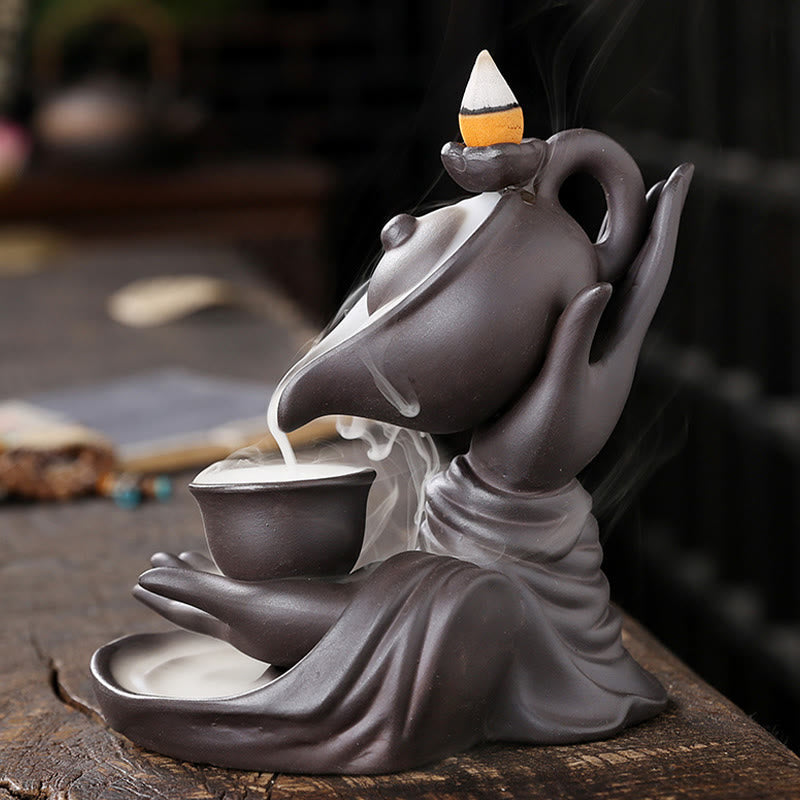 Buddha Hand Teapot Incense Burner – Tilted teapot pours smoke into shallow bowl, draped sleeve base, ceramic