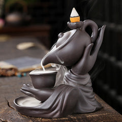 Buddha Hand Teapot Incense Burner – Tilted teapot pours smoke into shallow bowl, draped sleeve base, ceramic