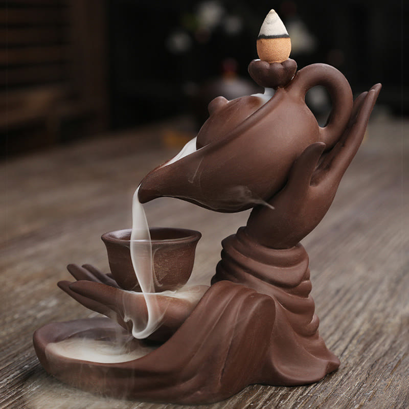 Buddha Hand Teapot Incense Burner – Brown clay teapot held by sculpted hand, smoke waterfall on wood