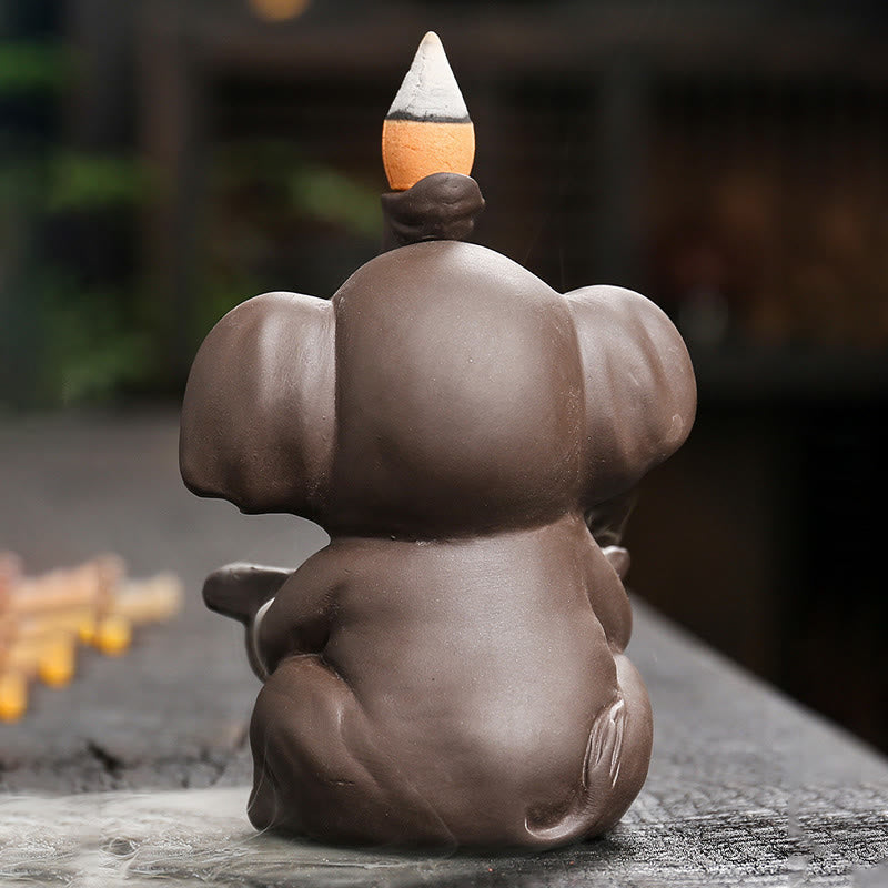 Elephant Backflow Incense Burner - Rear three-quarter view on stone with foliage background, purple clay censer