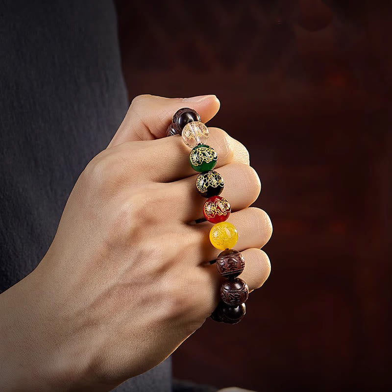 Five Directions Wealth Bracelet - Worn on hand showing carved wood and five-color deity beads, rich burgundy backdrop