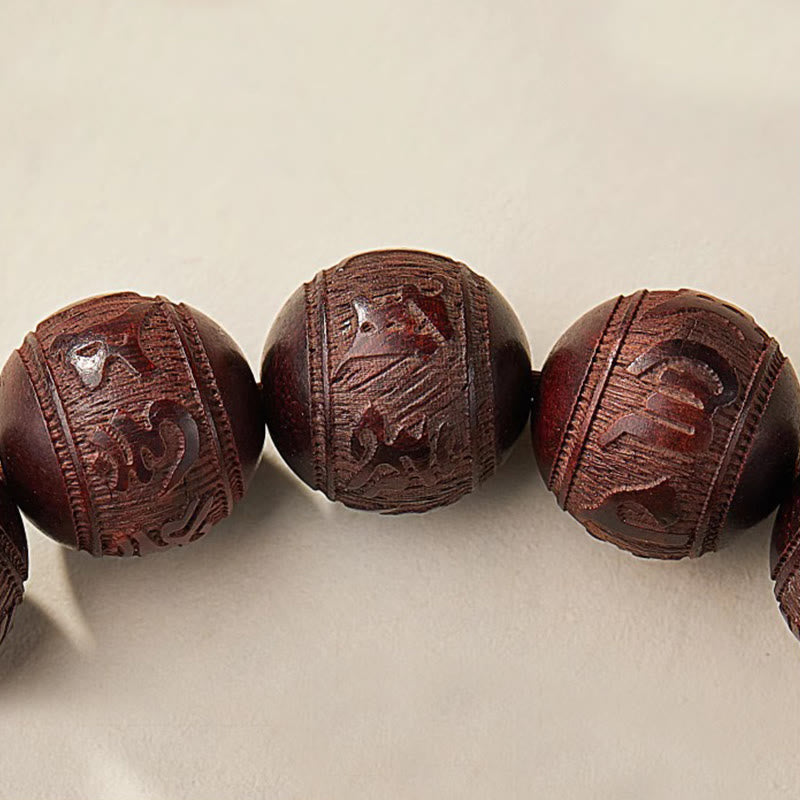 Five Directions Wealth Bracelet - Macro detail of carved sandalwood beads with intricate relief mantra, wood grain