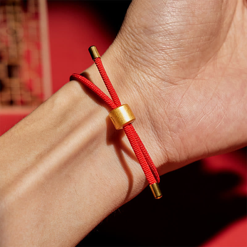 Red cord bracelet worn on wrist with gold sliding bead closure, lifestyle photography with burgundy background and architectural elements