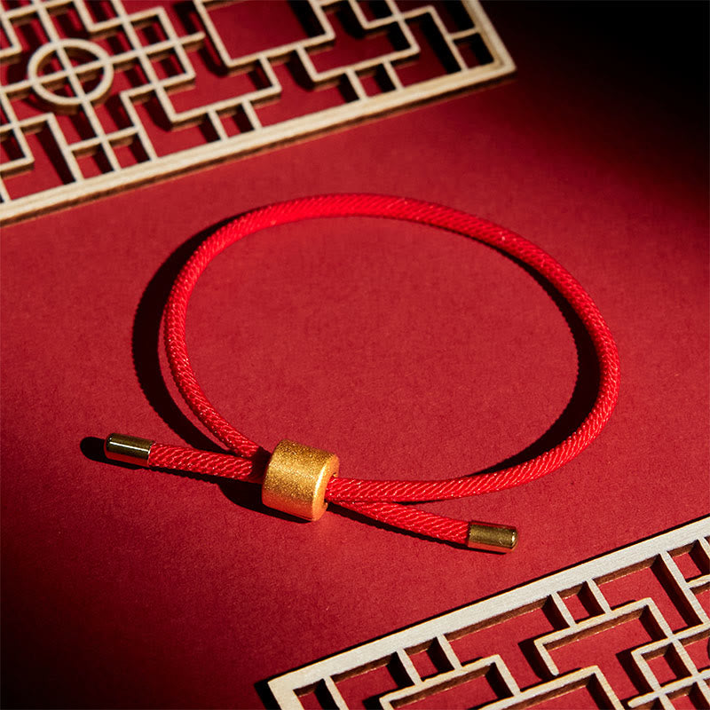Lucky red string bracelet with gold sliding bead closure, braided crimson cord on red display with traditional Chinese lattice frames