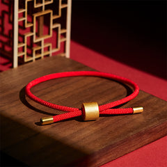 Red string bracelet with gold adjustable sliding bead, displayed on dark walnut wood with traditional Chinese geometric lattice screen background