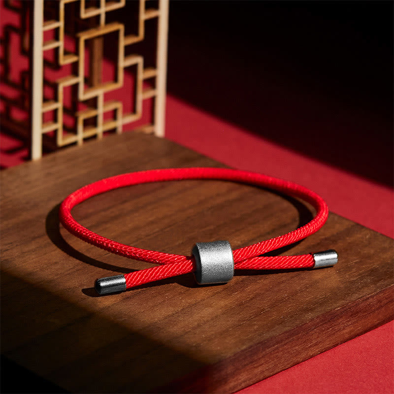 Adjustable red cord bracelet with brushed silver sliding bead closure, minimalist lucky string design on wooden display with golden lattice background
