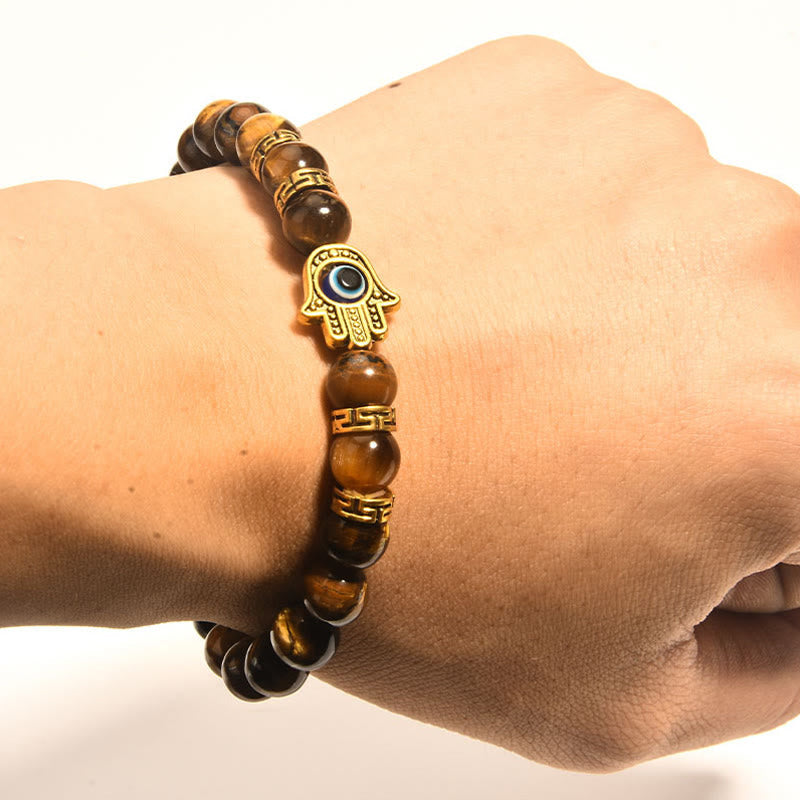 Tiger eye stretch bracelet with gold Hamsa evil eye focal charm, dark stone display