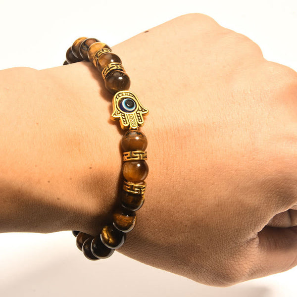 Tiger eye stretch bracelet with gold Hamsa evil eye focal charm, dark stone display