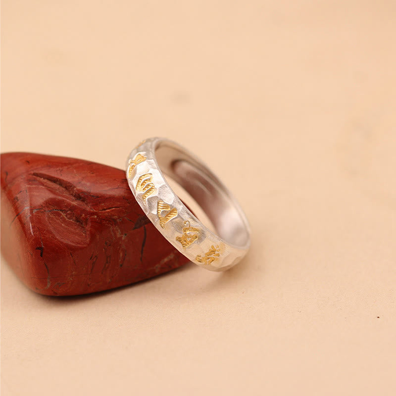 Hammered Om Mani Padme Hum Ring - angled on polished stone with gold symbols, zen silver band