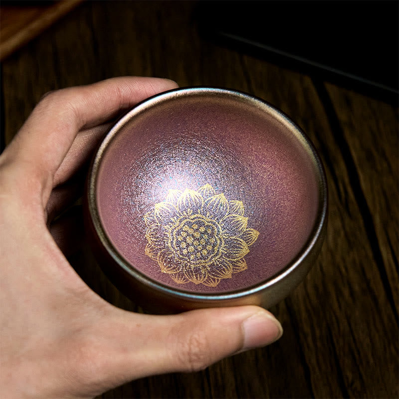 Golden Lotus Ceramic Tea Cup – held in hand showing purple iridescent glaze with gold lotus, Jianzhan