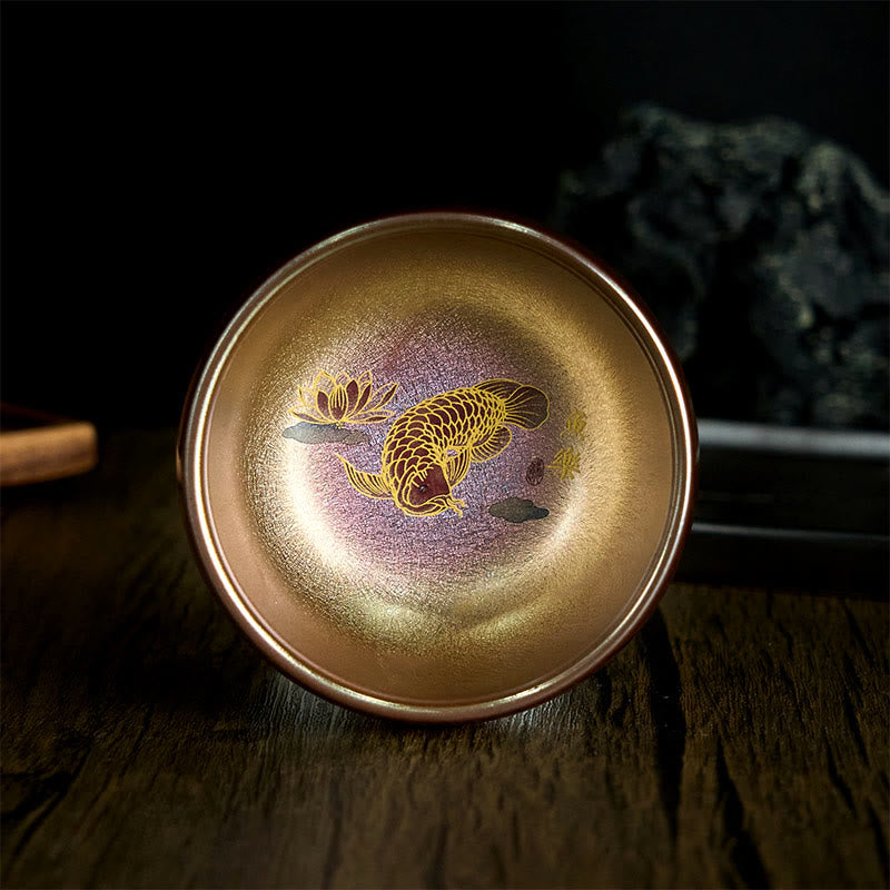 Jianzhan Koi Fish Lotus Teacup – golden-bronze iridescent glaze, gold koi and lotus interior, dark wood, angled top view