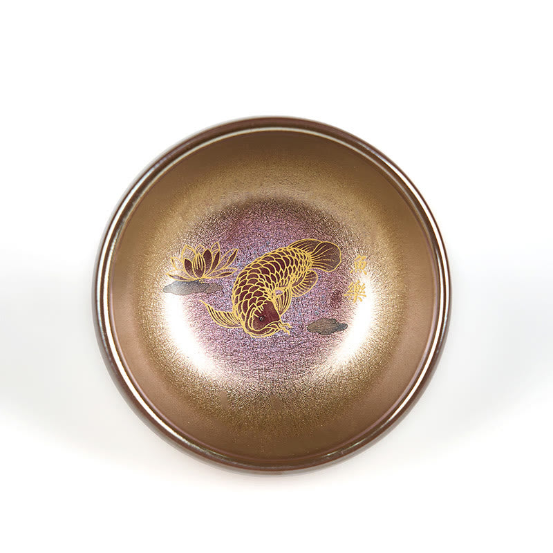 Jianzhan Koi Fish Lotus Teacup – overhead on white background, bronze-gold iridescent, gold koi fish and lotus, purple center