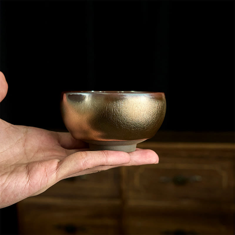 Jianzhan Koi Fish Lotus Teacup – copper-bronze iridescent bowl held in hand, textured metallic glaze, black background
