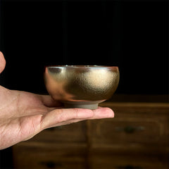 Jianzhan Koi Fish Lotus Teacup – copper-bronze iridescent bowl held in hand, textured metallic glaze, black background
