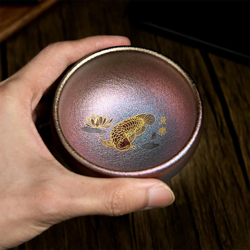 Jianzhan Koi Fish Lotus Teacup – angled view on dark wood, metallic bronze-purple iridescent, koi and lotus motif