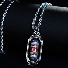Om Mani Padme Hum Prayer Wheel Pendant – Angled on warm wood surface, revealing twisted rope chain and colored enamel barr...
