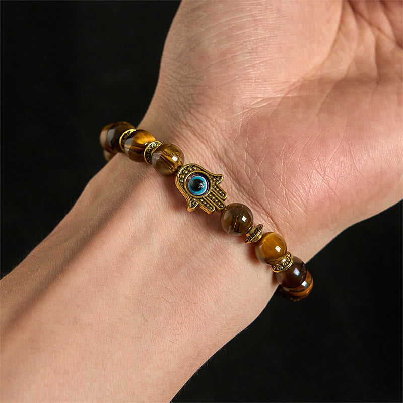 Tiger eye bead bracelet with Hamsa evil eye charm and gold spacer beads on white background