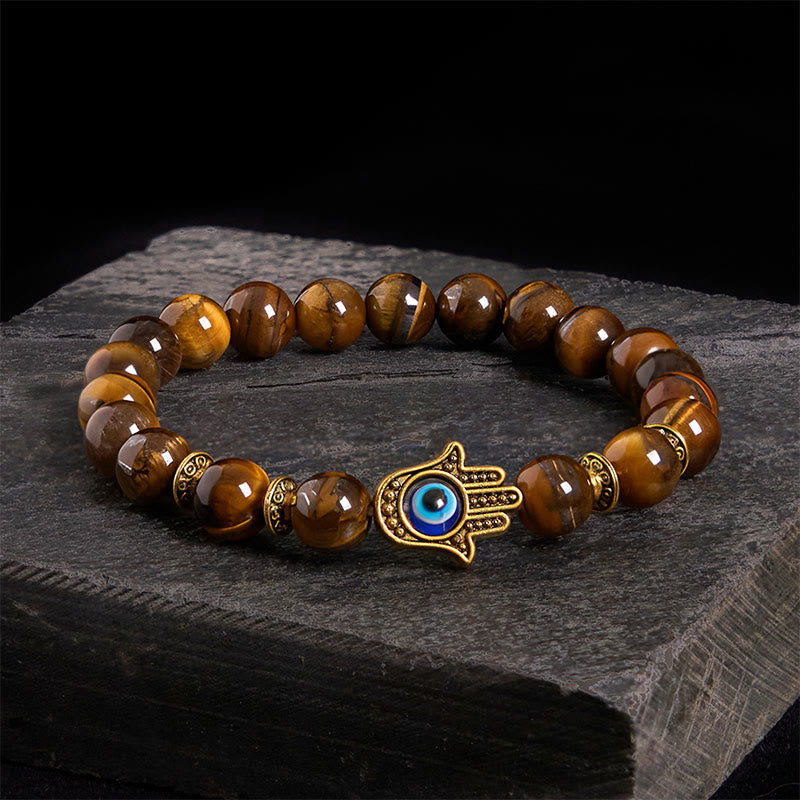 Tiger eye beaded bracelet with gold Hamsa hand evil eye charm on dark slate stone background