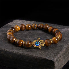 Tiger eye beaded bracelet with gold Hamsa hand evil eye charm on dark slate stone background