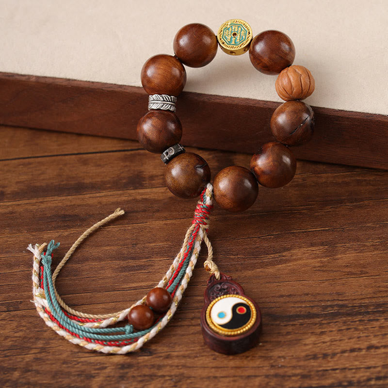 Tibet Jujube Wood Yin Yang Bracelet – three-quarter view on dark wood showing gold medallion, carved wood beads and yin-ya...