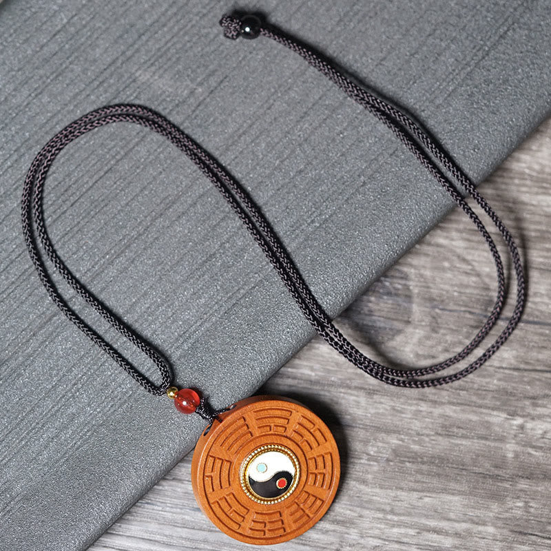 Jujube Wood Yin Yang Bagua Necklace – Flat lay of carved wood bagua necklace with red carnelian bead on gray textile, spir...