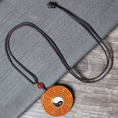 Jujube Wood Yin Yang Bagua Necklace – Flat lay of carved wood bagua necklace with red carnelian bead on gray textile, spir...