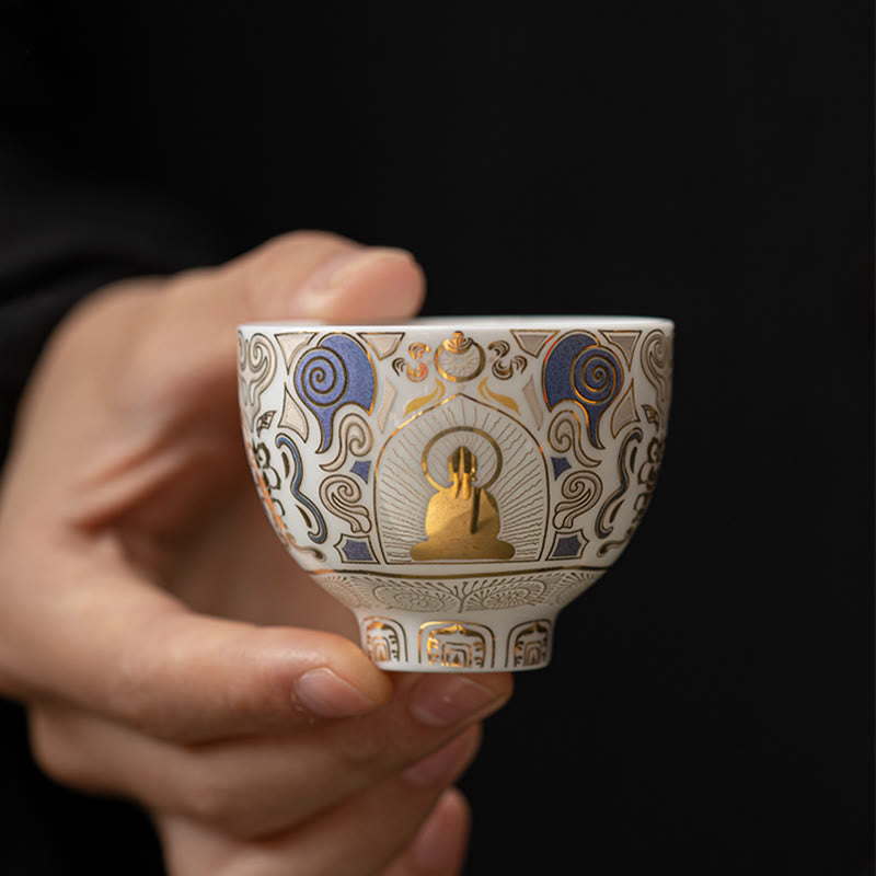 White Thangka Buddha Kung Fu Tea Cup – side view in hand against black background, intricate gold Thangka patterns, detail