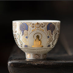 White Thangka Buddha Kung Fu Tea Cup – front view on dark wooden stand, gold Buddha with halo on white porcelain, studio shot