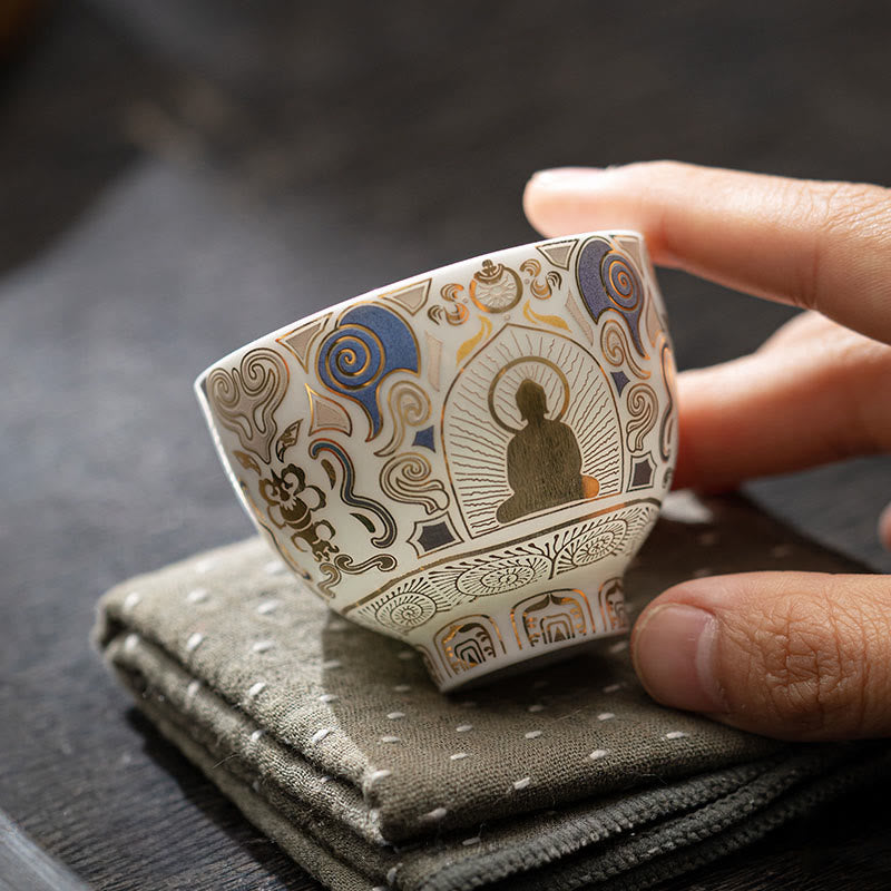 White Thangka Buddha Kung Fu Tea Cup – angled view on grey dotted napkin, gold Buddha and ornate cloud motifs, craftsmanship