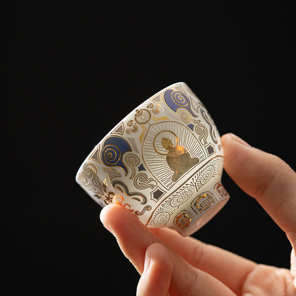 White Thangka Buddha Kung Fu Tea Cup – hand-held side view showing gold Buddha and blue clouds on white ceramic, closeup detail