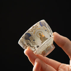 White Thangka Buddha Kung Fu Tea Cup – hand-held side view showing gold Buddha and blue clouds on white ceramic, closeup detail