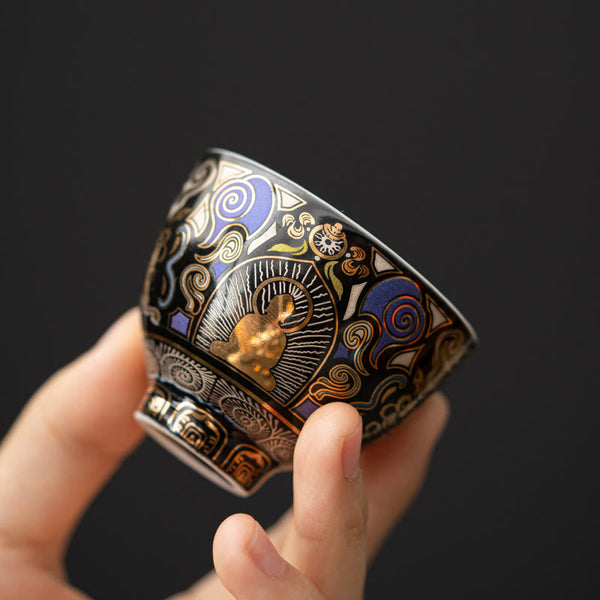 Black Thangka Buddha Kung Fu Tea Cup – hand-held side view showing gold Buddha and blue cloud motifs on black ceramic, closeup detail