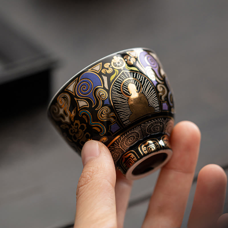 Black Thangka Buddha Kung Fu Tea Cup – angled side view in hand against grey surface, gold Buddha with ornate cloud patterns