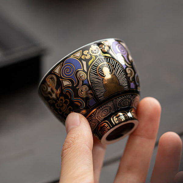 Black Thangka Buddha Kung Fu Tea Cup – angled side view in hand against grey surface, gold Buddha with ornate cloud patterns