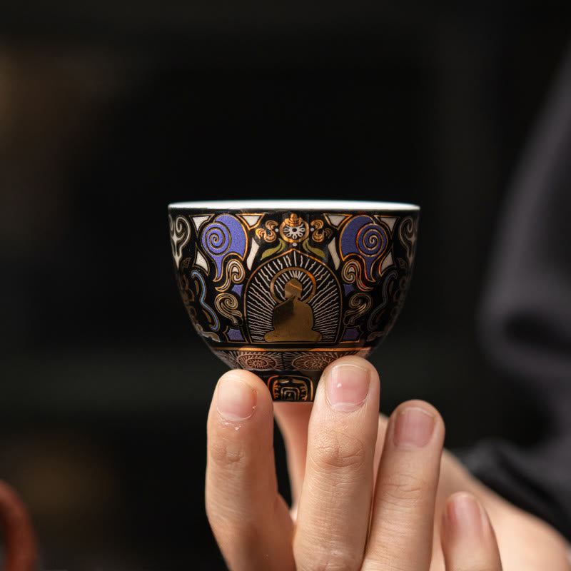 Black Thangka Buddha Kung Fu Tea Cup – front view held by fingertips against dark background, delicate porcelain craftsmanship