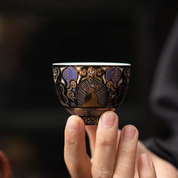 Black Thangka Buddha Kung Fu Tea Cup – front view held by fingertips against dark background, delicate porcelain craftsmanship