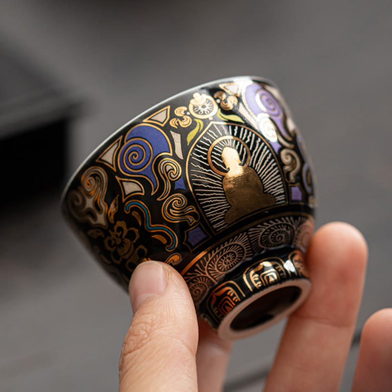 Black Thangka Buddha Kung Fu Tea Cup – angled 45-degree view in hand showing base detail and gold patterns, craftsmanship