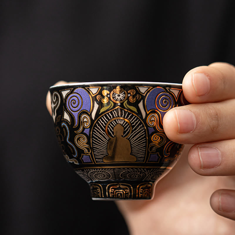Black Thangka Buddha Kung Fu Tea Cup – two hands holding front view, gold Buddha figure with blue auspicious clouds, serene