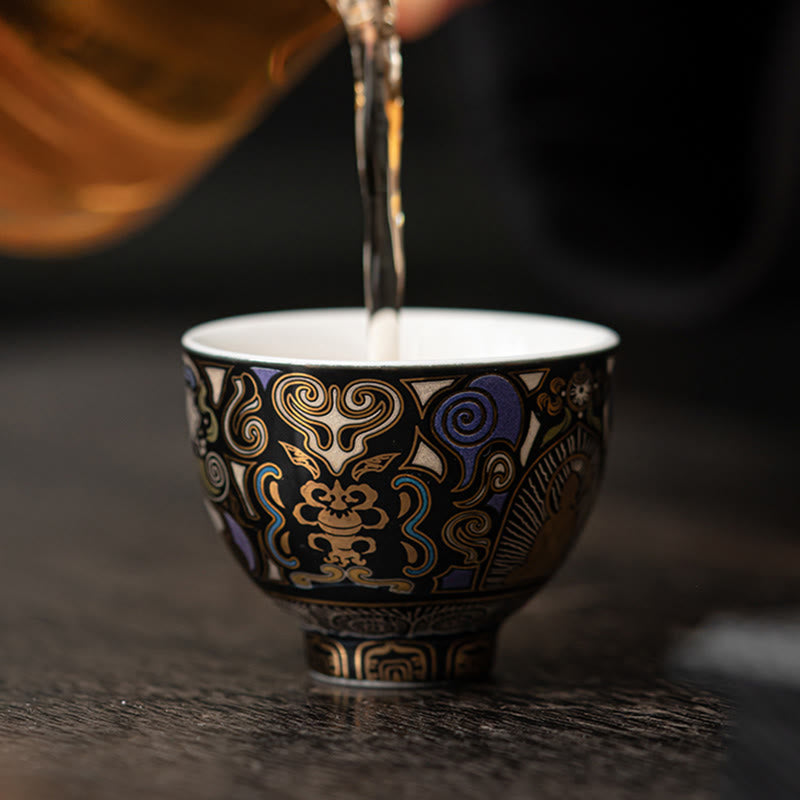 Black Thangka Buddha Kung Fu Tea Cup – tea being poured into cup on dark wooden table, golden liquid, mindful tea ritual