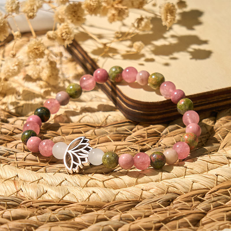 Pink rose quartz and green stone beaded bracelet with silver lotus centerpiece on woven mat, crystal healing