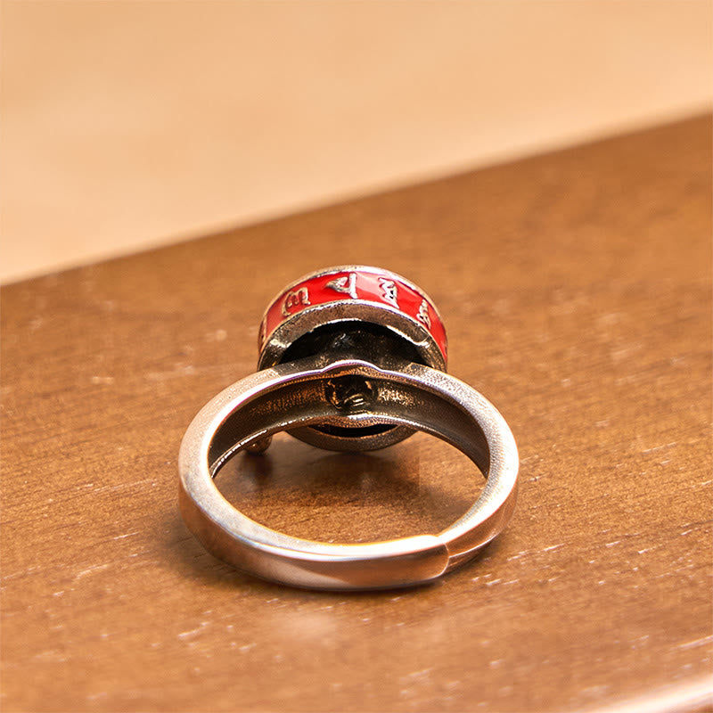 Copper Prayer Wheel Ring - Rear angle on dark wood showing oxidized band and rotating red mantra barrel, worry ring