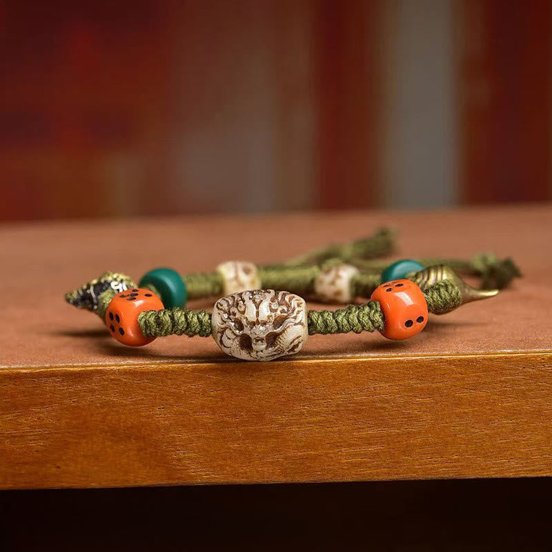 Tibetan Dragon Dice Bone Rope Bracelet – close-up carved dragon bead with orange dice on wood, Protection